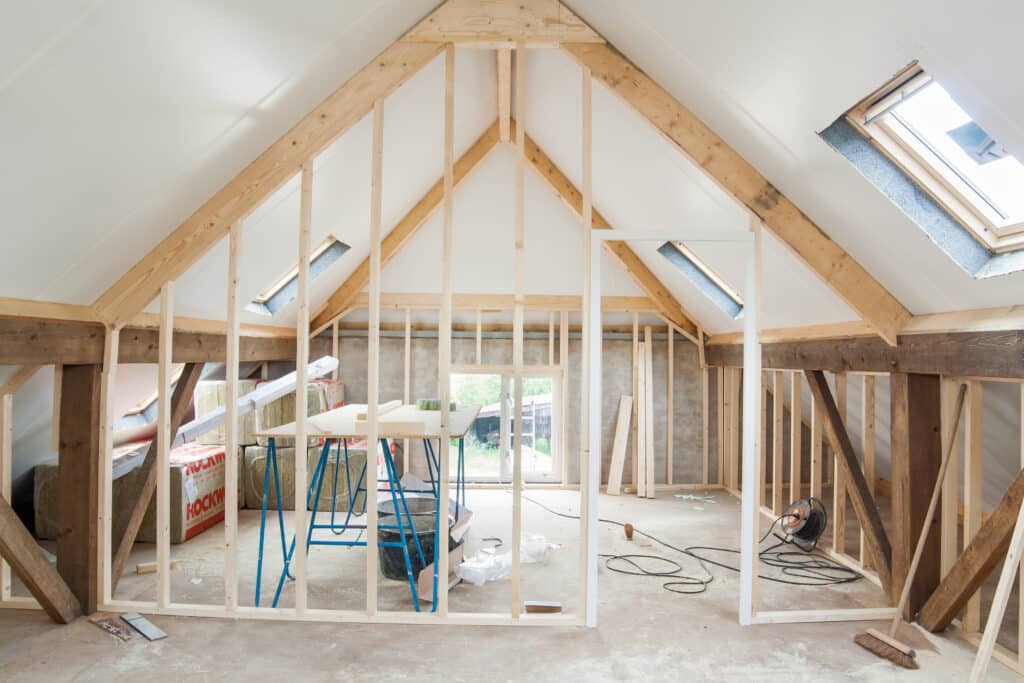 Aménagement intérieur d'un grenier en construction, avec charpente bois, fenêtres de toit, et isolation ROCKWOOL au sol.