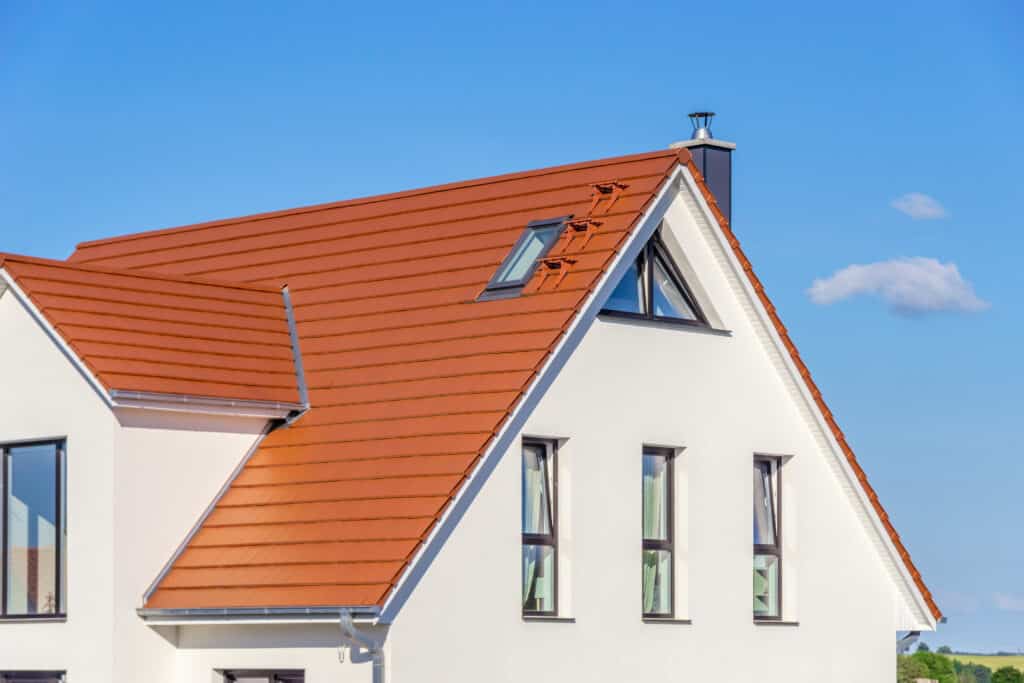 Toiture en tuiles orange et façade blanche d'une maison moderne sous un ciel bleu. Cheminée et lucarne visibles.
