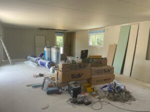 Chantier de rénovation intérieure avec isolation KNAUF, sacs SFV et Eco Soft, plaques de plâtre et outils divers sur sol brut.