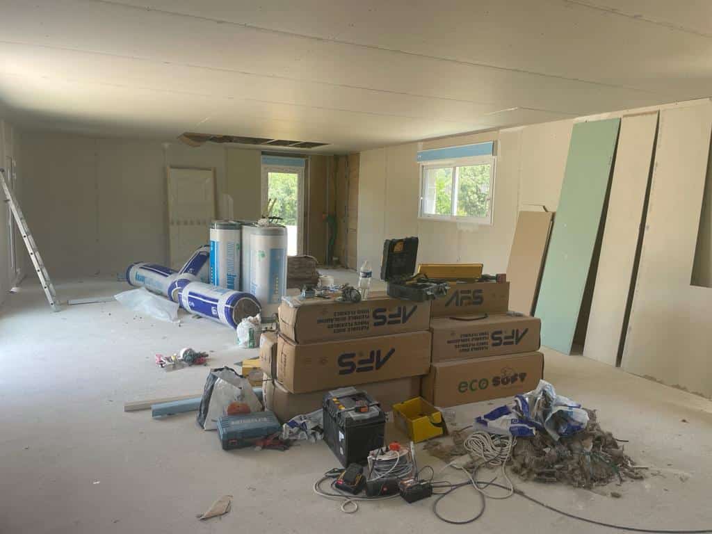 Chantier de rénovation intérieure avec isolation KNAUF, sacs SFV et Eco Soft, plaques de plâtre et outils divers sur sol brut.