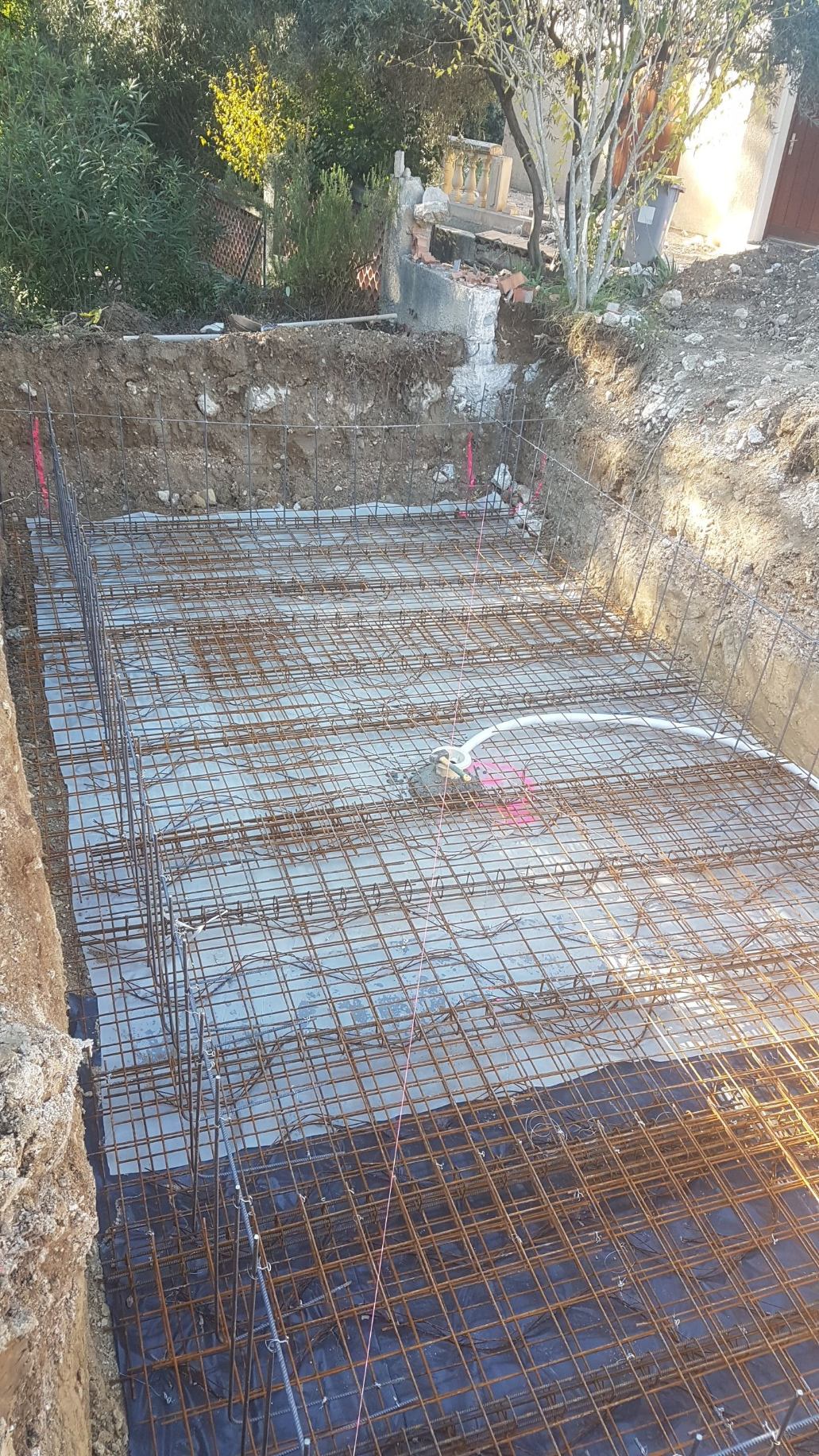 Armatures métalliques posées pour la dalle d'une piscine en cours de construction, avec tuyauterie visible.