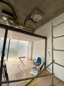 Rénovation d'une salle : plafond béton brut avec unités CVC exposées. Poutre métallique et sol protégé par du carton Lidl.