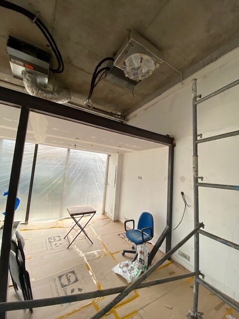 Rénovation d'une salle : plafond béton brut avec unités CVC exposées. Poutre métallique et sol protégé par du carton Lidl.
