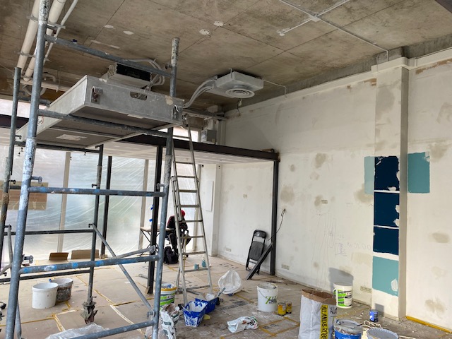 Rénovation : choix des couleurs et préparation du chantier. Rénovation intérieure : échafaudage métallique, plafond en béton brut, unité de CVC et échantillons de peinture turquoise sur mur.