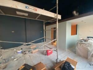 Chantier de rénovation avec échafaudage Camabi. Murs peints en bleu canard profond et vert pâle, contrastant avec une niche orange. Outils Hilti.