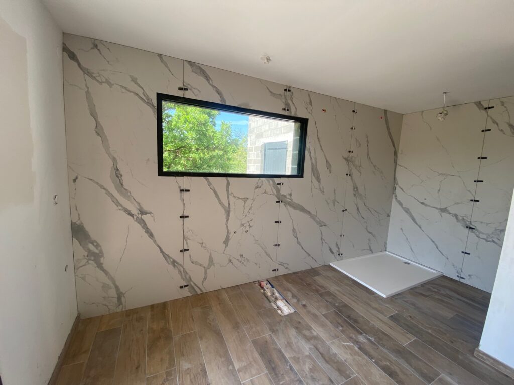 Pose de grands carreaux effet marbre et sol imitation bois dans une salle de bain lumineuse en chantier.