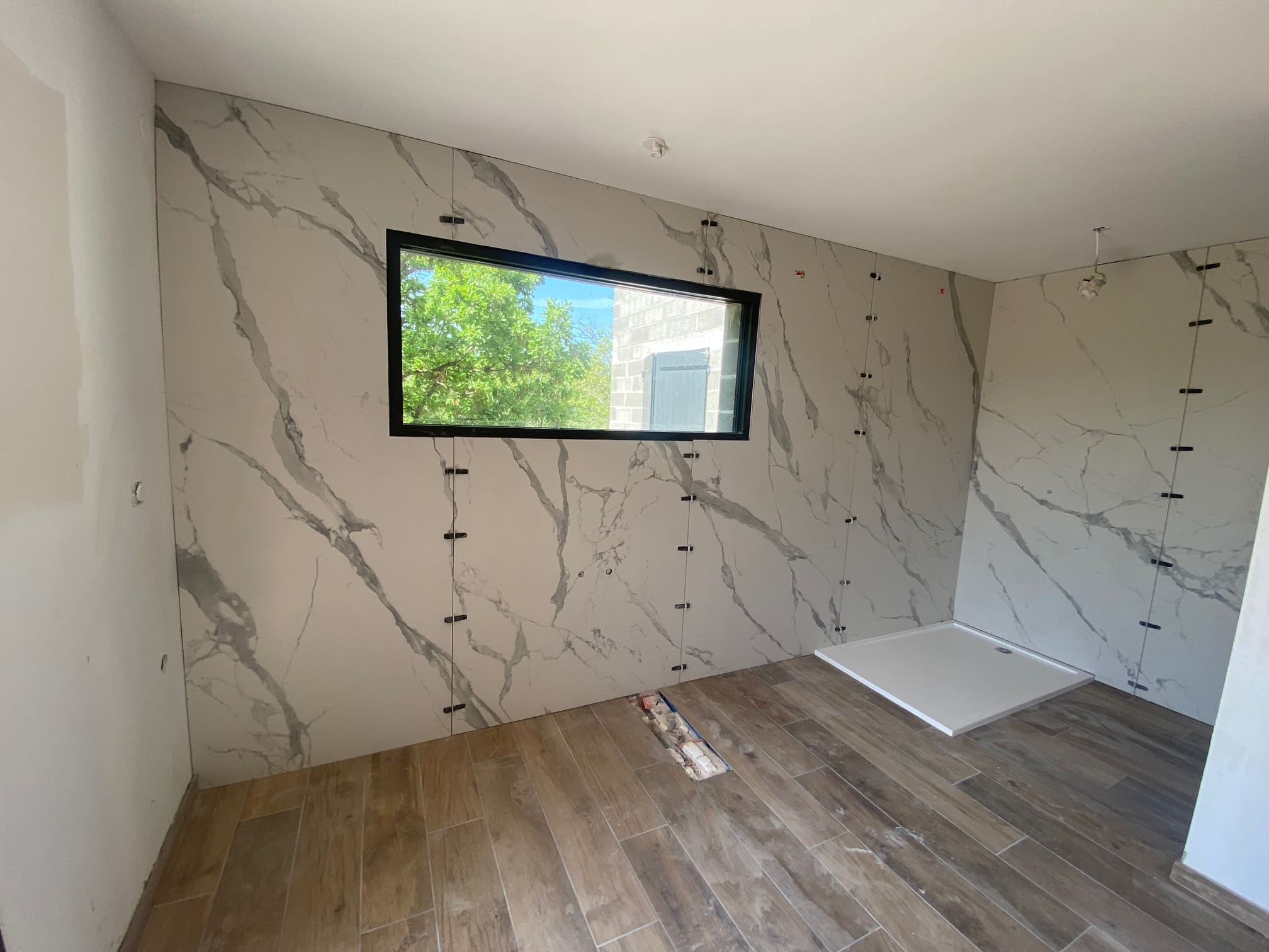 Pose de grands carreaux effet marbre et sol imitation bois dans une salle de bain lumineuse en chantier.