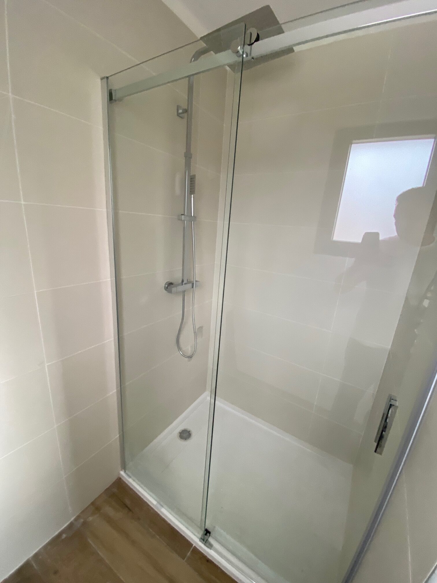 Douche à l'italienne avec paroi en verre coulissante, robinetterie chromée et carrelage beige dans salle de bain moderne.