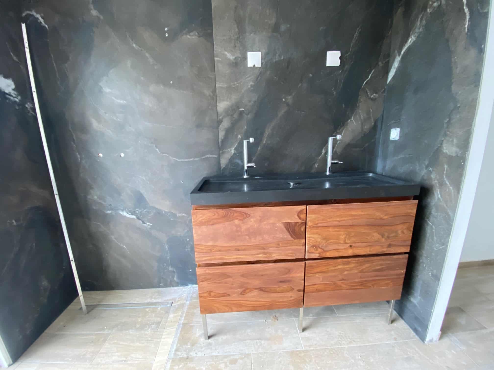 Meuble vasque double en bois et pierre noire devant un mur en marbre sombre dans une salle de bain moderne.