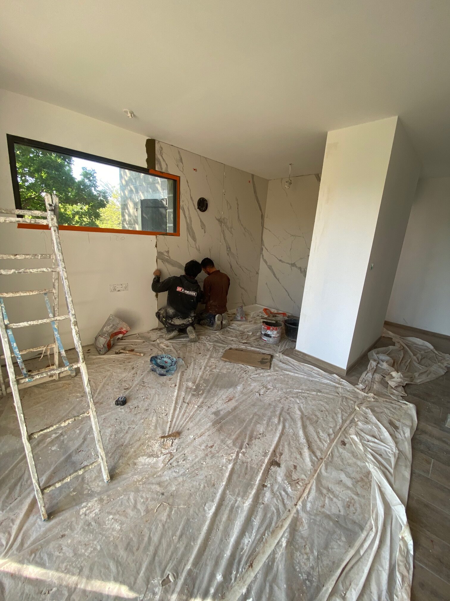 Deux ouvriers installent de grands carreaux effet marbre dans une pièce en rénovation avec matériel Parkside.