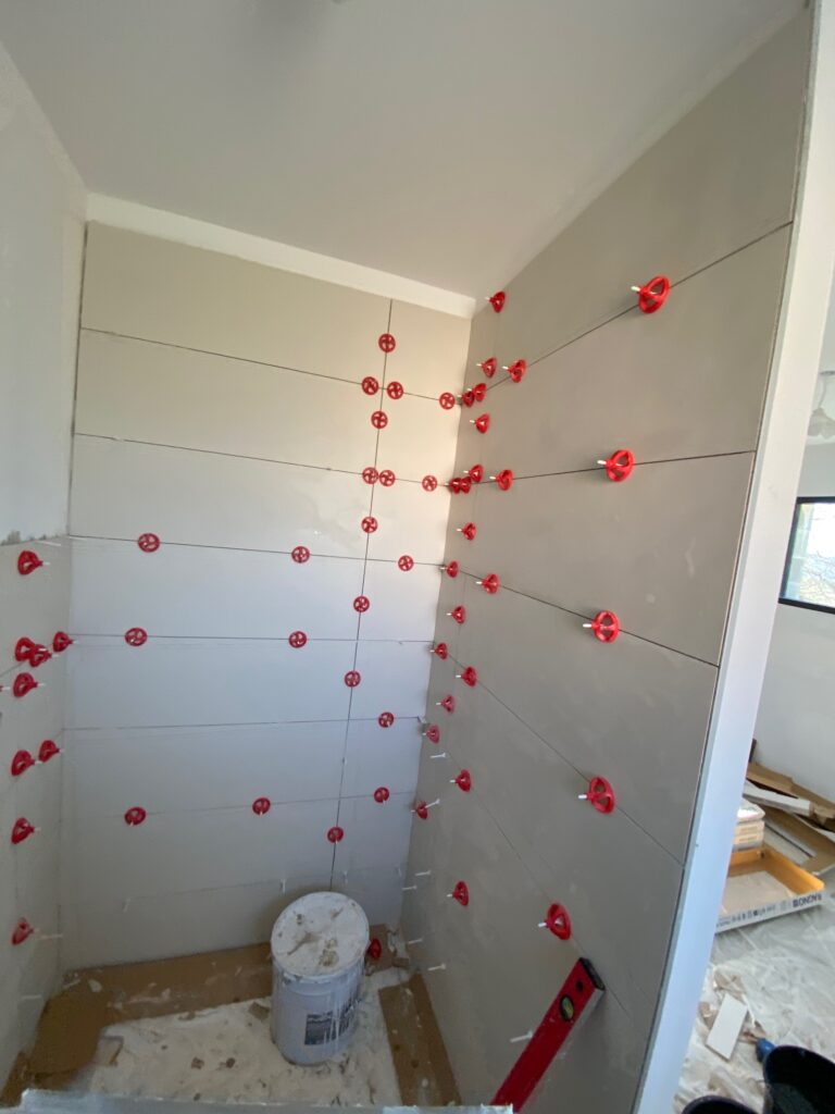 Pose carrelage mural avec système autonivelant rouge Pose de carrelage mural grand format avec croisillons autonivelants rouges dans une salle de bain en rénovation.