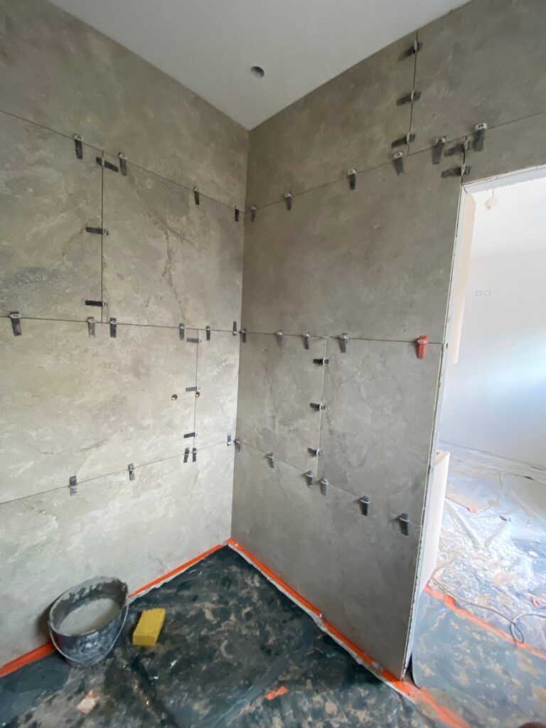 Pose de grands carreaux effet pierre avec croisillons de nivellement dans une douche en cours de travaux.