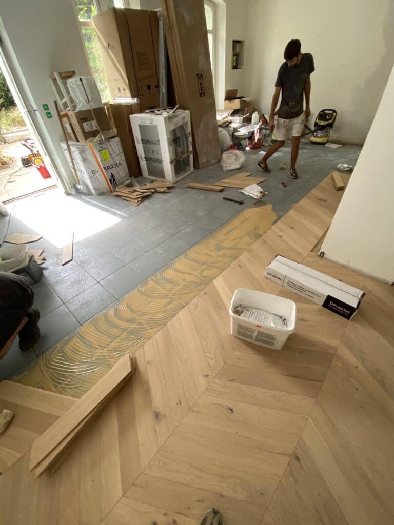 Pose de parquet en chêne chevron Décoplus Parquets sur carrelage gris lors d'une rénovation intérieure.