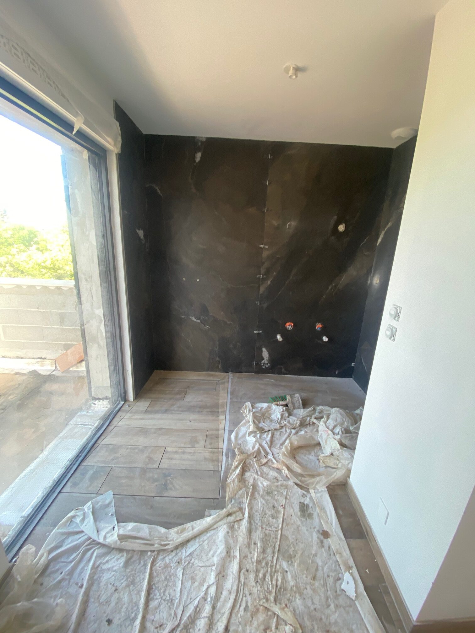 Rénovation de salle de bain : carrelage mural marbre noir, sol aspect bois et baie vitrée lumineuse.