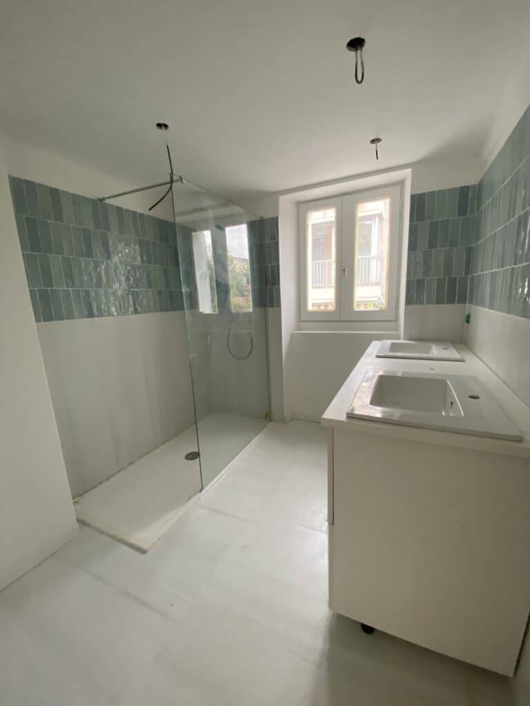 Salle de bain moderne en rénovation avec douche à l'italienne vitrée, double vasque blanche et carrelage mural bleu.