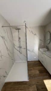 Salle de bain moderne avec douche à l'italienne en marbre blanc, double vasque et sol effet bois chaleureux.