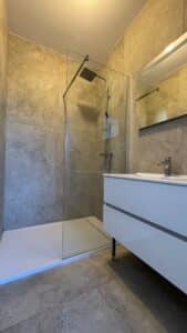 Salle de bain moderne avec douche à l'italienne, carrelage gris pierre et meuble vasque blanc design.