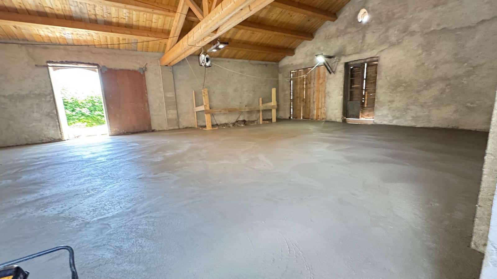 Dalle de béton fraîchement coulée dans un bâtiment rustique avec poutres en bois apparentes.