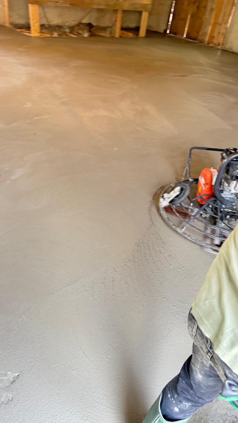 Lissage d'une dalle en béton frais avec une truelle mécanique sur un chantier intérieur.