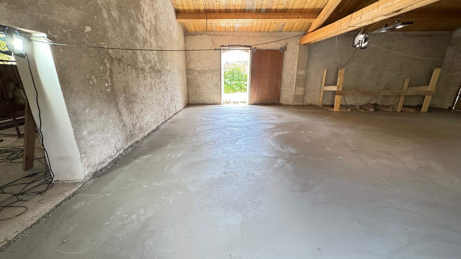 Sol en béton lisse dans une grange en rénovation avec charpente bois apparente.
