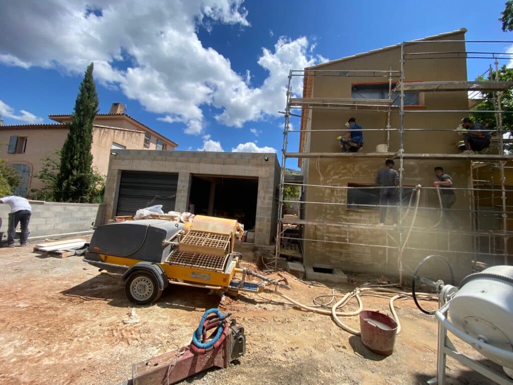 Ravalement de façade : Chantier de rénovation et enduit Chantier de ravalement de façade avec ouvriers sur échafaudage et machine à projeter l'enduit extérieur.